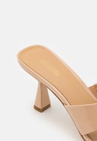 Sandale beige pour femmes Michael Kors avec un bout carré, un talon évasé de hauteur moyenne et une large bride sur le dessus du pied.
