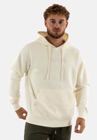 Sweatshirt à capuche couleur crème avec un tissage texturé, poche kangourou et cordons de serrage. Comprend une broderie de logo subtile à l'avant.