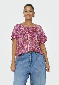 Un haut à manches courtes texturé en rose et violet avec un motif géométrique, associé à un jean en denim bleu ample.