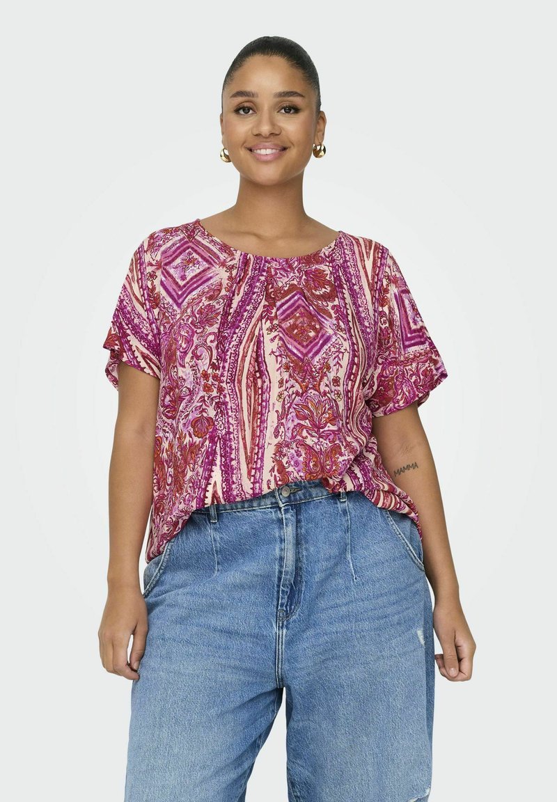 Un haut à manches courtes texturé en rose et violet avec un motif géométrique, associé à un jean en denim bleu ample.