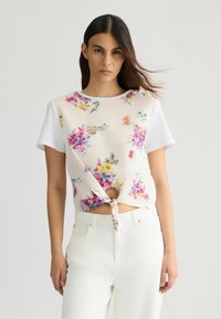 Blomsterprintet kortærmet top med knude detalje ved taljen, lavet af letvægtsstof med en cremefarvet baggrund og farverige blomster mønstre.