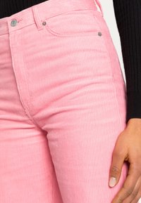 Rosa kordfloretbyxor med subtil vertikal ribbning, hög midja och silverfärgad knapprad vid midjan.