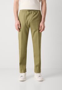 Ljus olivgröna byxor med elastisk midja och dragband, med framvikningar och rak bendesign, stylat med vita sneakers.