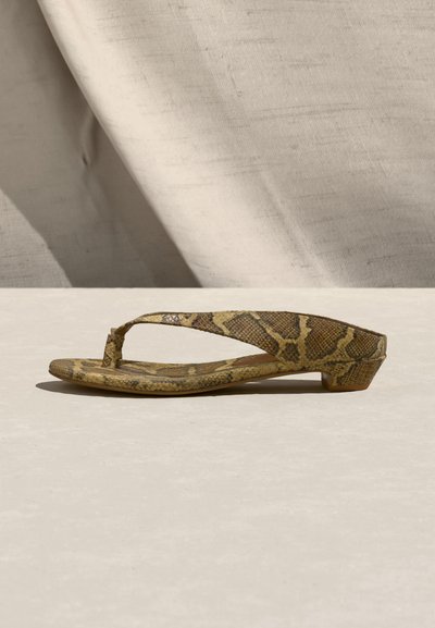 Καφέ και μπεζ φλατ σανδάλι με σχέδιο φίδιου δέρματος, χαμηλό τακούνι, λουράκι ανάμεσα στα δάχτυλα και στρογγυλεμένη τετράγωνη μύτη, εκτεθειμένο σε ανοιχτή επιφάνεια.