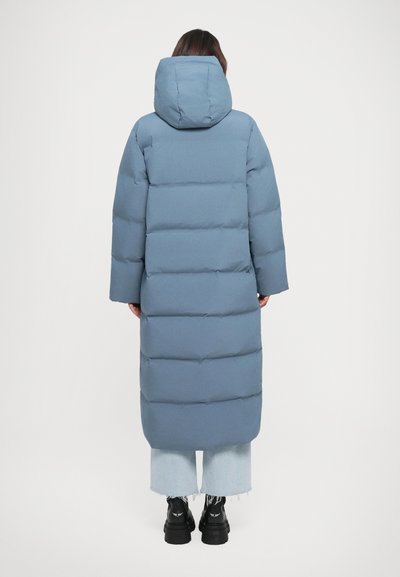 Long, puffer coat in light blue, featuring a hood and wide sleeves, with horizontal stitching. Paired with light denim jeans and black boots.