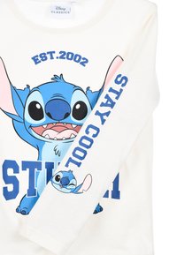 Weißes Langarmshirt mit einem blauen Cartoon-Charakter mit großen Augen. Textdrucke "STITCH" und "STAY COOL" in Blau. Aus weichem Baumwollmaterial.