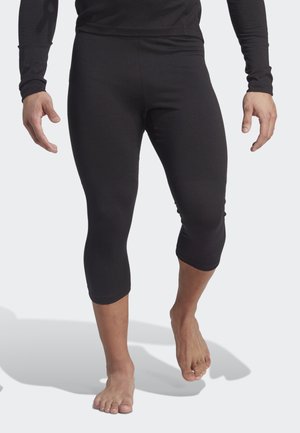 Leggings deportivos negros hechos de un tejido elástico, cortos a mitad de pantorrilla. Textura suave con un diseño ajustado. La modelo está descalza.
