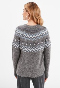 Grijze gebreide trui met een pattered schouder in blauw en wit, ronde hals en ribgebreide onderrand. Zachte textuur met een relaxte pasvorm.
