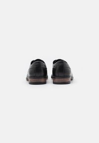 Schwarze Lederschuhe mit einer glatten Oberfläche, runden Zehen und einer kontrastierenden strukturierten braunen Sohle mit einem dezenten Muster.