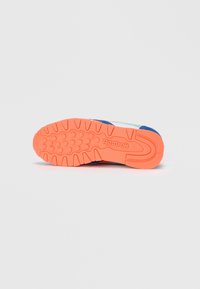 Suela naranja de una zapatilla Reebok azul y blanca con agarre texturizado y logo de Reebok, vista desde abajo sobre un fondo blanco.