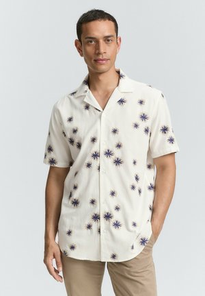 Chemise à manches courtes en tissu blanc avec un motif étoilé bleu et jaune, dotée d'un col décontracté et d'un ourlet droit.