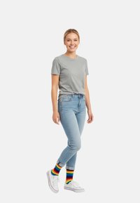 Graues Baumwoll-T-Shirt, hellblaue Skinny-Jeans und weiße Sneakers mit bunten, gestreiften Socken. Einfaches Design, lässige Passform, lebendige Farbakzente.