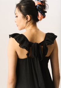 Black dress with ruffled sleeves, open back, and tied detail. Made of textured fabric, featuring subtle pleats and a flowing silhouette.
