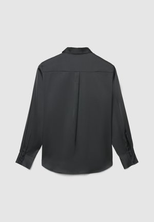 Schwarze Langarmbluse mit Rückenteil, mittiger Falte und ärmellangen Manschetten, auf einem schlichten hellgrauen Hintergrund präsentiert.