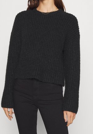 Maglione nero a coste con scollatura a girocollo, maniche a campana lunghe e orlo leggermente accorciato. Tessuto morbido e vestibilità rilassata.