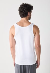 Débardeur sans manches blanc en tissu côtelé doux. Il présente un col arrondi et un ourlet droit, avec une texture lisse.