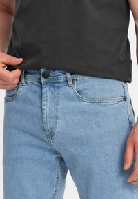 Jeans de denim azul claro con corte recto, que cuentan con un cierre clásico de botón y costuras en contraste a lo largo de los bolsillos y las costuras.