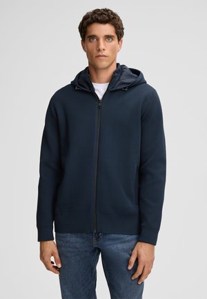 Marineblaues Zip-Hoodie mit strukturiertem Oberflächenmaterial, verstellbarer Kapuze und seitlichen Taschen. Der Stoff wirkt leicht und leger, ideal zum Schichten.