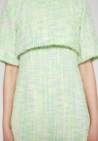 Haut à manches courtes texturé vert clair et blanc et jupe taille haute assortie sur une personne aux bras nus.