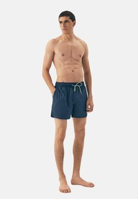 Granatowe szorty kąpielowe wykonane z lekkiego materiału, z elastycznym paskiem w talii, sznurkiem oraz bocznymi kieszeniami.