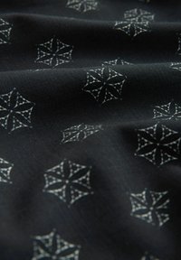 Tissu noir avec des motifs géométriques d'étoiles blanches répétées, montrant des plis doux et une texture.