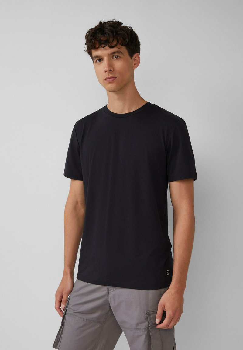 Zwart katoenen T-shirt met korte mouwen, ronde hals en een simpele uitstraling. Heeft een klein logo aan de onderzijde. Draagt met grijze cargoshorts.