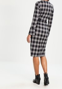 Svart och vit rutmönstrad långärmad klänning med figurnära design, knälång längd, och matchad med svarta ankelboots.