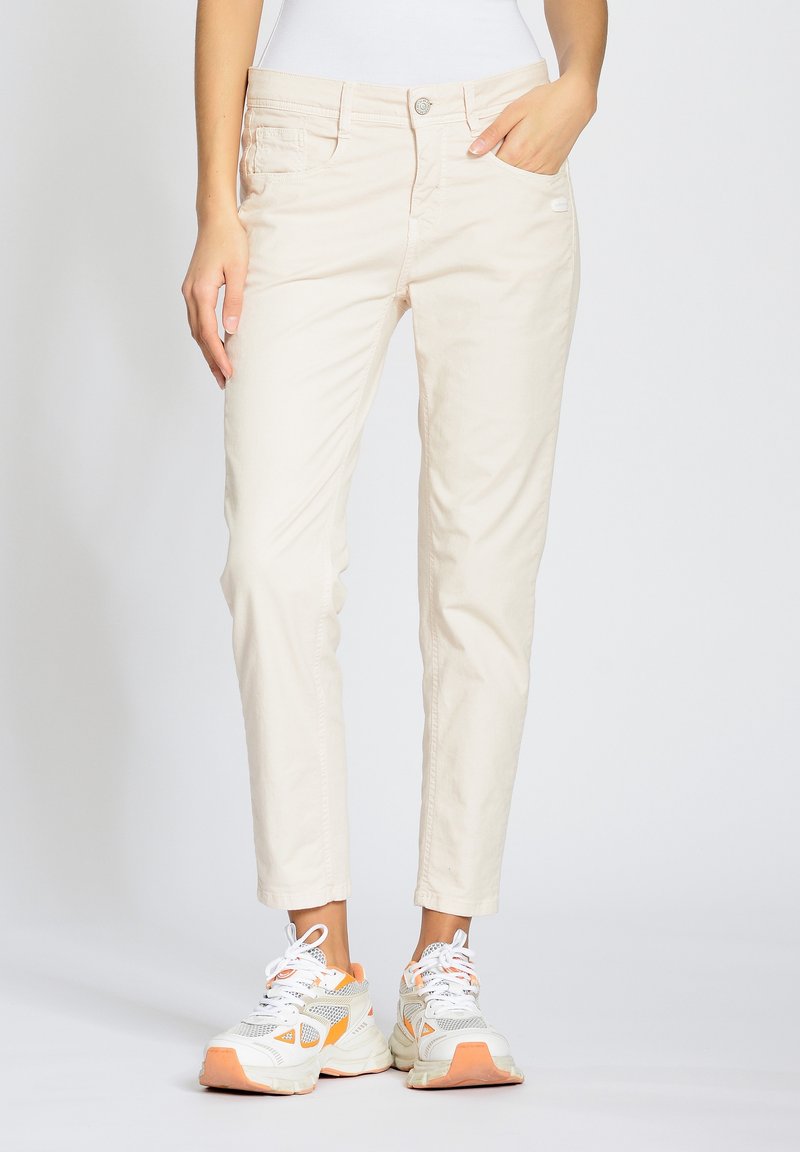 Pantalones de algodón beige con un corte ajustado, que cuentan con bolsillos frontales y cierre de botón. Combinados con zapatillas deportivas blancas y naranjas.