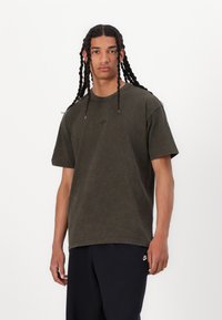 Tricou din bumbac de culoare verde măsliniu, cu guler rotund, mâneci scurte și un logo Nike minimal brodat pe piept; textură moale, croială confortabilă.