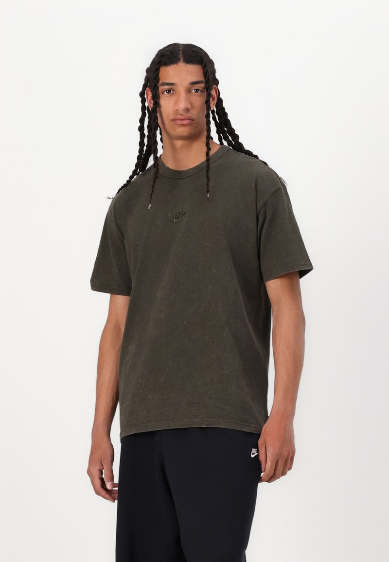 Tricou din bumbac de culoare verde măsliniu, cu guler rotund, mâneci scurte și un logo Nike minimal brodat pe piept; textură moale, croială confortabilă.