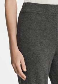 Grijze brei-broek heeft een zachte textuur en een elastische tailleband, met een close-up van de stof en een hand die op het been rust.