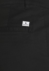 Tessuto di cotone nero con una superficie liscia, dotato di una tasca e di un'etichetta bianca con la scritta "JACK & JONES" in testo nero.