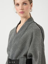 Prenda en blanco y negro con diseño cruzado, que muestra una textura geométrica y un cinturón negro contrastante con herrajes metálicos.