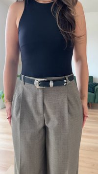Schwarzes ärmelloses Top, kombiniert mit hochgeschnittenen grauen gemusterten Hosen, akzentuiert durch einen strukturierten schwarzen Gürtel mit einer silbernen Schnalle.