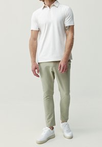 Hvit polo skjorte med halv-glidelås krage, paret med lysegrønne slim-fit bukser og hvite sneakers. Enkelt design, glatt tekstur.