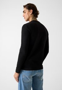 Zwarte longsleeve gemaakt van zacht materiaal, voorzien van een ronde hals en een aansluitend ontwerp. Gecombineerd met lichtblauwe spijkerbroek.