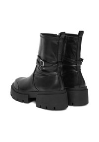 Melnu ādas potītes zābaku pāris ar masīvām zoleēm, sānu rāvējslēdzi un dekoratīvām sprādzēm uz baltas fona.