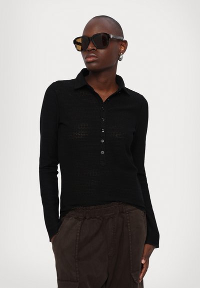 Sort langærmet polo-shirt med knap-front, struktureret strikmønster og krave, parret med mørkebrun, afslappet pasform bukser.