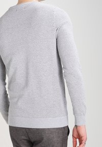Szary dziergany sweter z teksturowanym wzorem, długimi rękawami i okrągłym dekoltem. Projekt uzupełniają ściągacze na mankietach i dole.