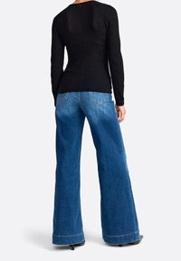 Schwarzes, geripptes Langarmshirt kombiniert mit weit geschnittenen, hellblauen Jeans mit leicht ausgefransten Säumen und sichtbaren Gesäßtaschen.