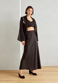 Svart satin tvådelat set med en kort topp och en flödande, högmidjad kjol. Accenterad med svarta skor med scallopkant.