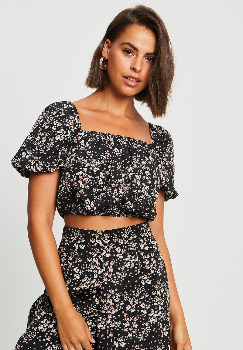 Haut court noir à fleurs avec de courtes manches bouffantes, présentant des motifs de fleurs multicolores, une taille élastique et un col carré.