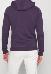Felpa con cappuccio di colore viola scuro, con cappuccio regolabile tramite cordoncino e polsini e orlo a costine. Tessuto morbido con una texture liscia, design minimalista.