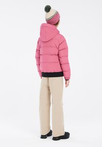 Giacca a vento rosa con cappuccio, caratterizzata da un trapuntato orizzontale e polsini elasticizzati. Abbinata a pantaloni beigi e scarpe con tacco nero.