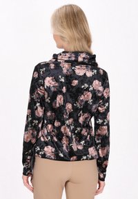 Top in morbido tessuto nero con un motivo floreale in tonalità di rosa e bianco, dotato di scollatura a cowl e maniche lunghe. Cuffie accentuate.