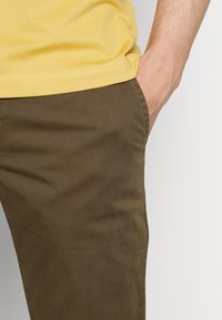Žluté tričko s texturovaným povrchem, doplněné hnědými bavlněnými kalhotami slim fit s bočními kapsami.