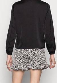 Sort satin langærmet top parret med en blomsterpræget, sort-hvid nederdel med flæsekanter, der viser en glat tekstur og figursyet design.