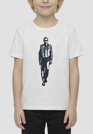 Bambino che indossa una maglietta bianca con una grafica in bianco e nero di una persona che cammina, con occhiali da sole e giacca.
