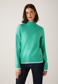 Türkiser Strickpullover mit hohem geripptem Kragen, langen Ärmeln und einem gerippten Saum, der am Bündchen und am unteren Rand einen weißen Akzent aufweist.