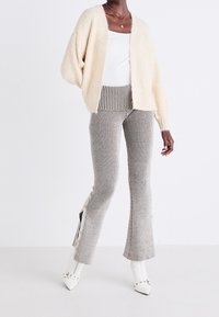 Oversized cream knit cardigan over a white top, paired with grey striped flared pants featuring side buttons and textured fabric.